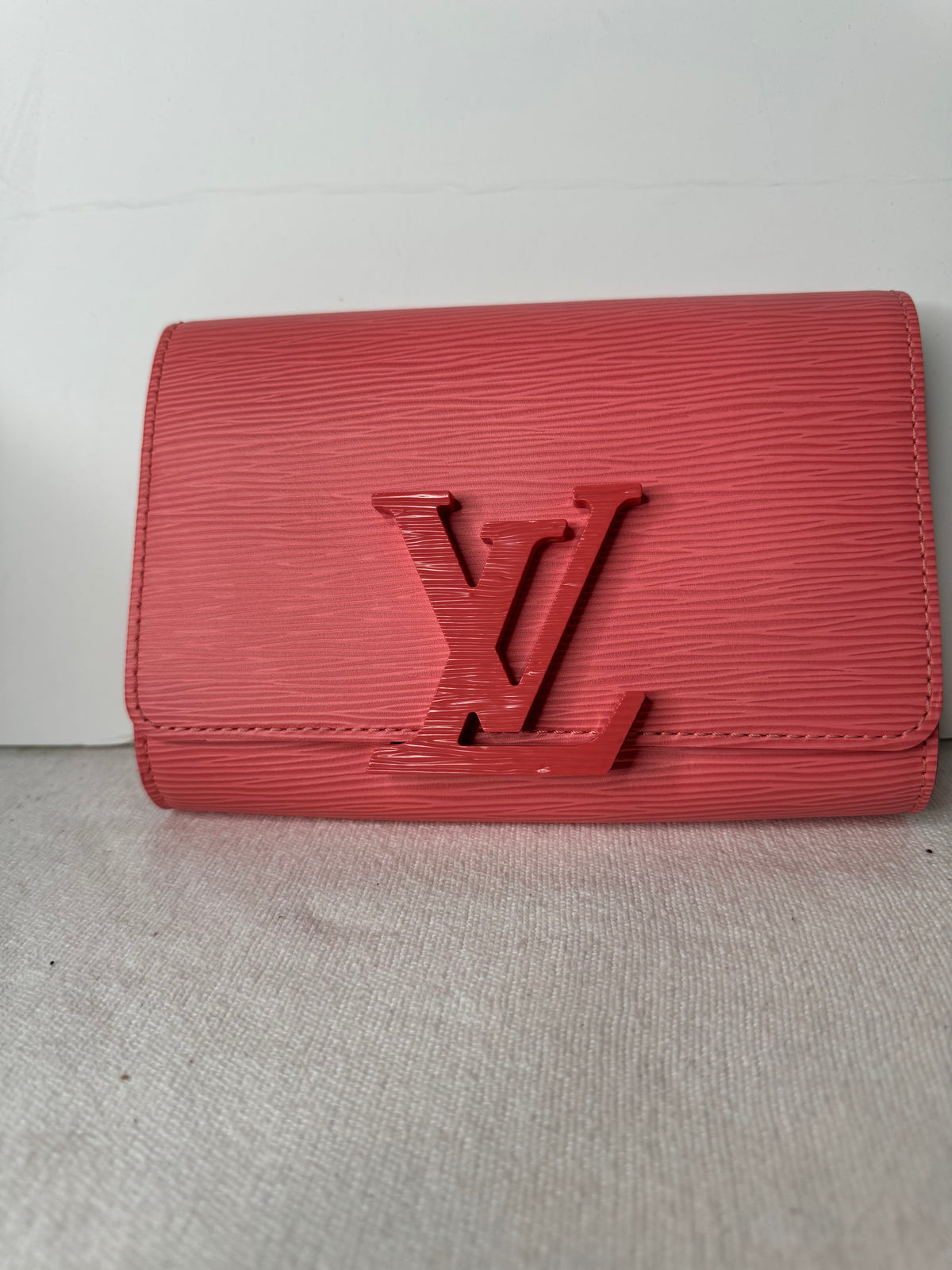 Front of coral-pink Louis Vuitton textured flap wallet with tonal LV detail