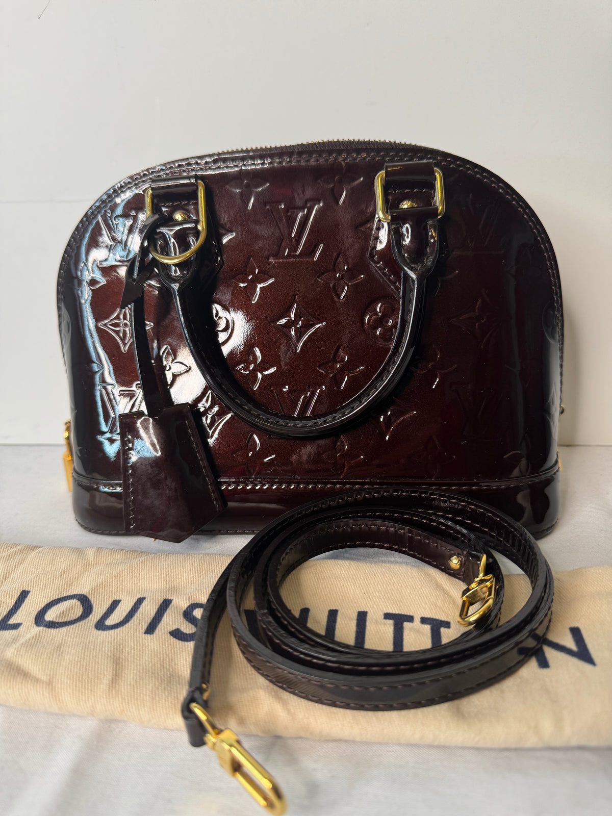 Burgundy Louis Vuitton monogram top handle bag photographed with a strap and dust bag