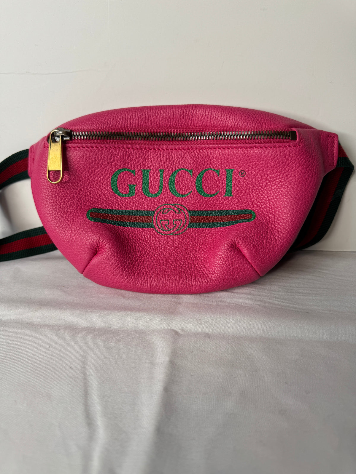 Pink Gucci logo belt bag with green-and-red striped strap and gold-tone zipper pull