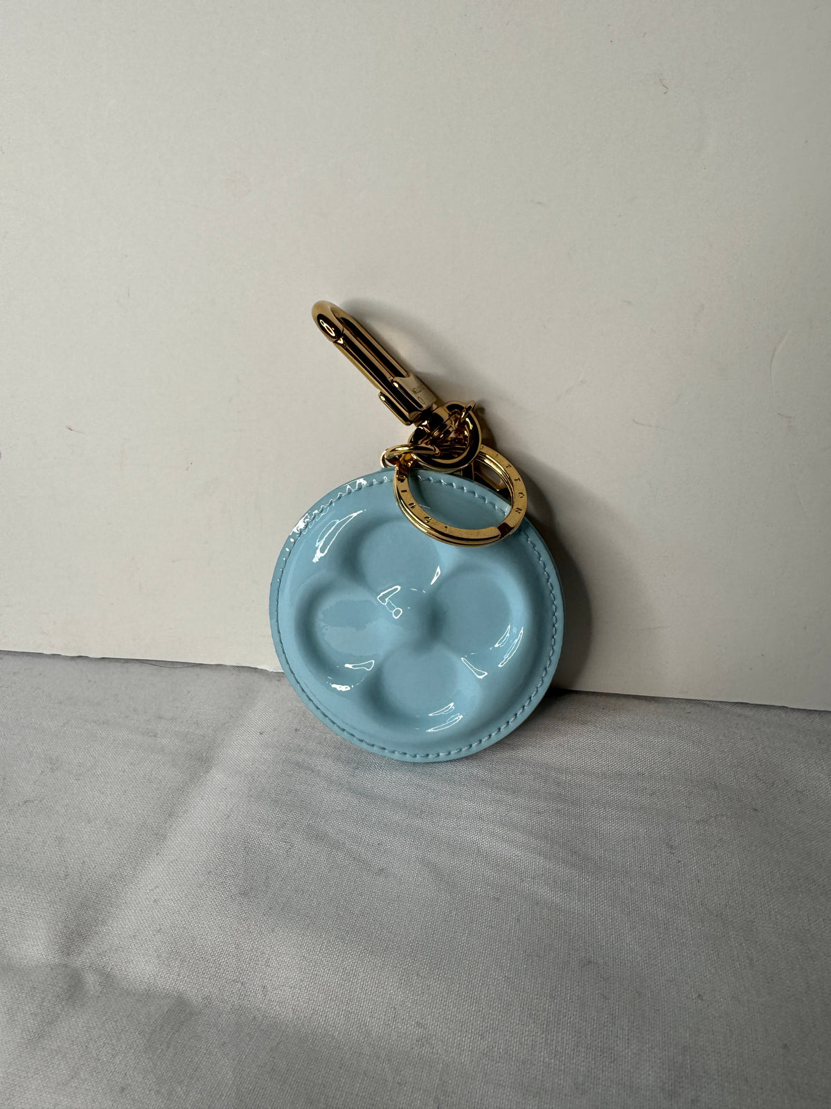 Light blue round bag charm with raised flower motif and gold-tone key ring and clasp