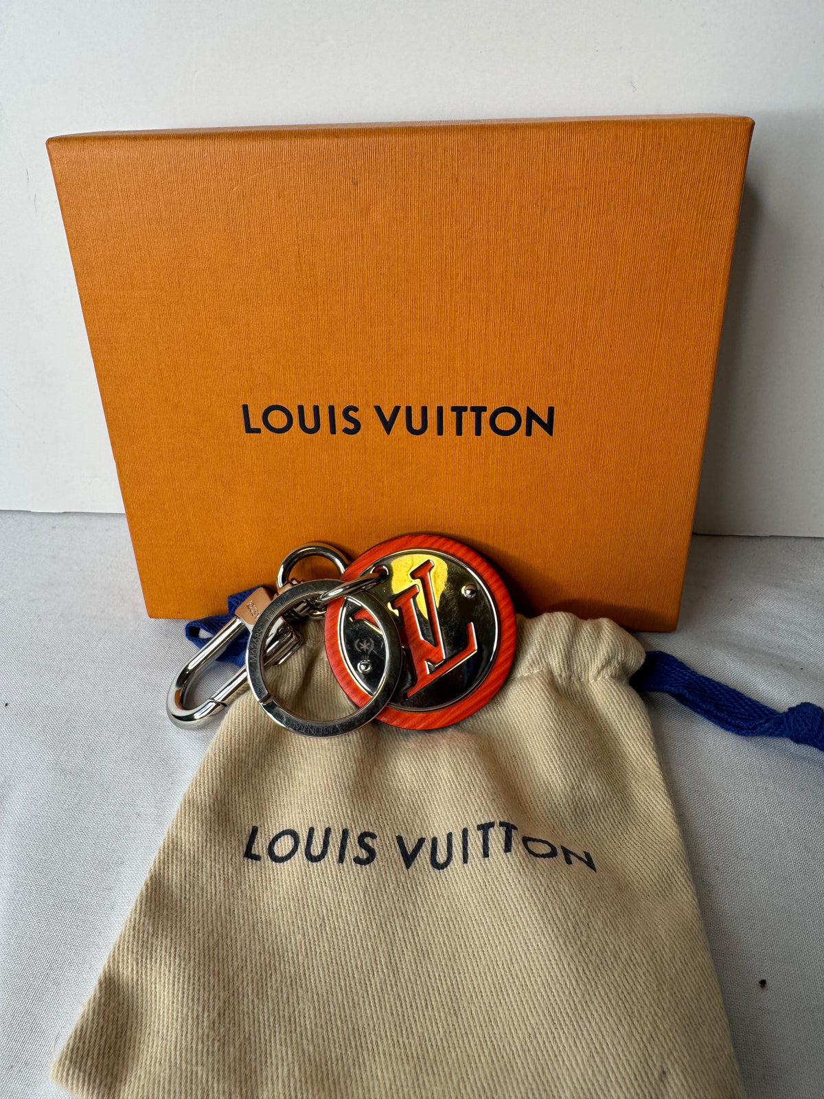 Louis Vuitton circular LV keychain with orange accents, silver-tone key ring and clasp, pictured with a box and dust pouch