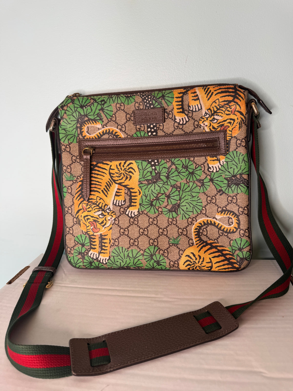 Gucci GG monogram messenger bag with orange tiger and green foliage print, brown trim, and green-and-red striped strap