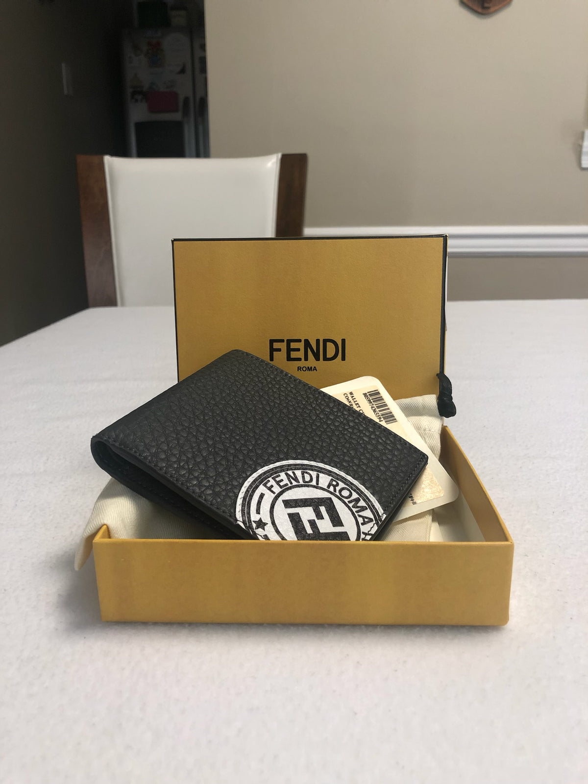 Black pebbled bifold wallet with white Fendi Roma stamp patch, held in hand